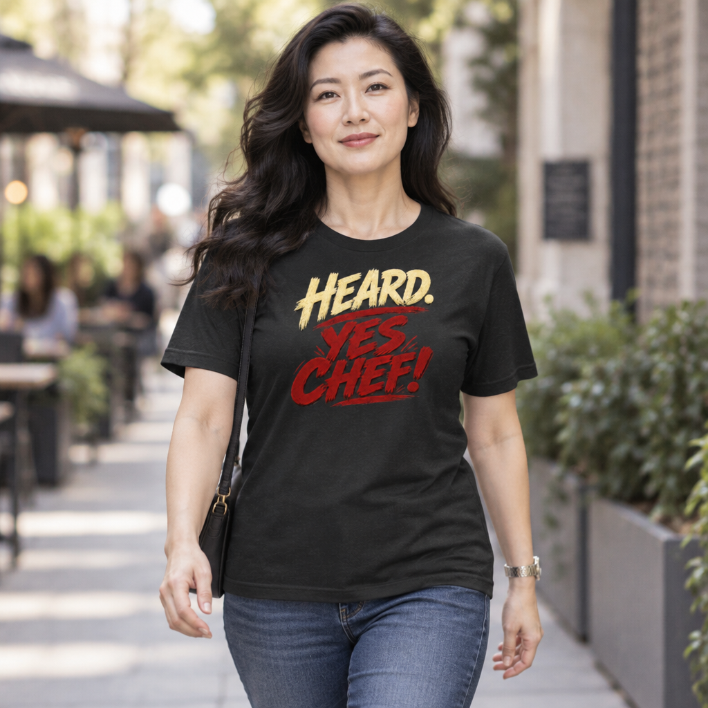 Lifestyle mockup of the Heard. Yes Chef! unisex T-shirt with cream and red brush lettering on black