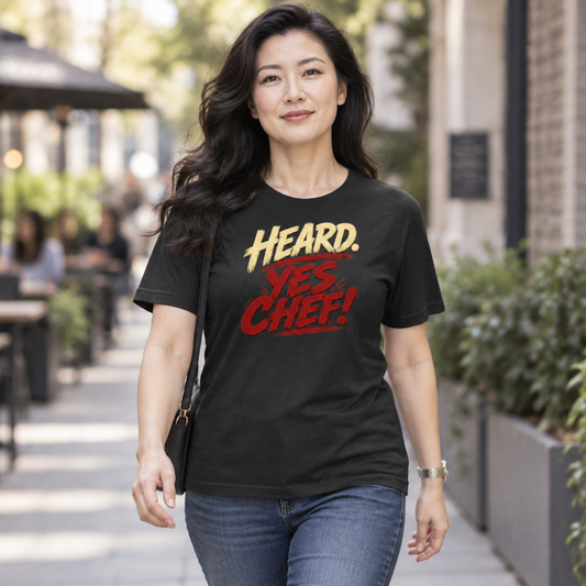 Lifestyle mockup of the Heard. Yes Chef! unisex T-shirt with cream and red brush lettering on black